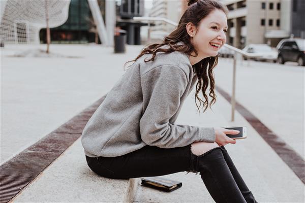 priscilla-du-preez-607207-unsplash Young woman holding phone and laughing.