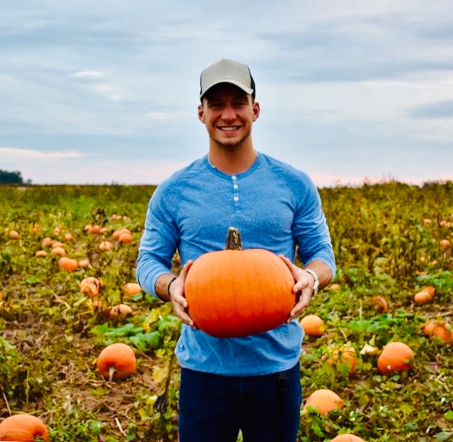 Man smiling and holding a pumpkin in a pumpkin patch.