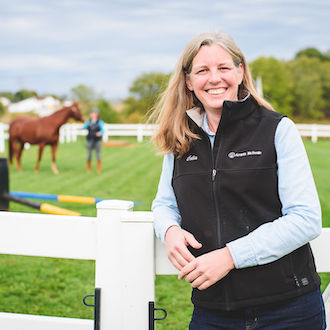 Woman smiling for camera with a horse in the background.