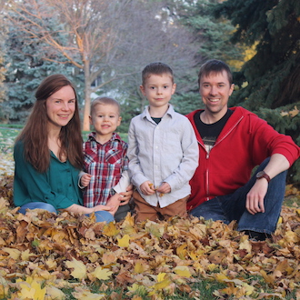 Family sitting in fall leaves and smiling for the camera.