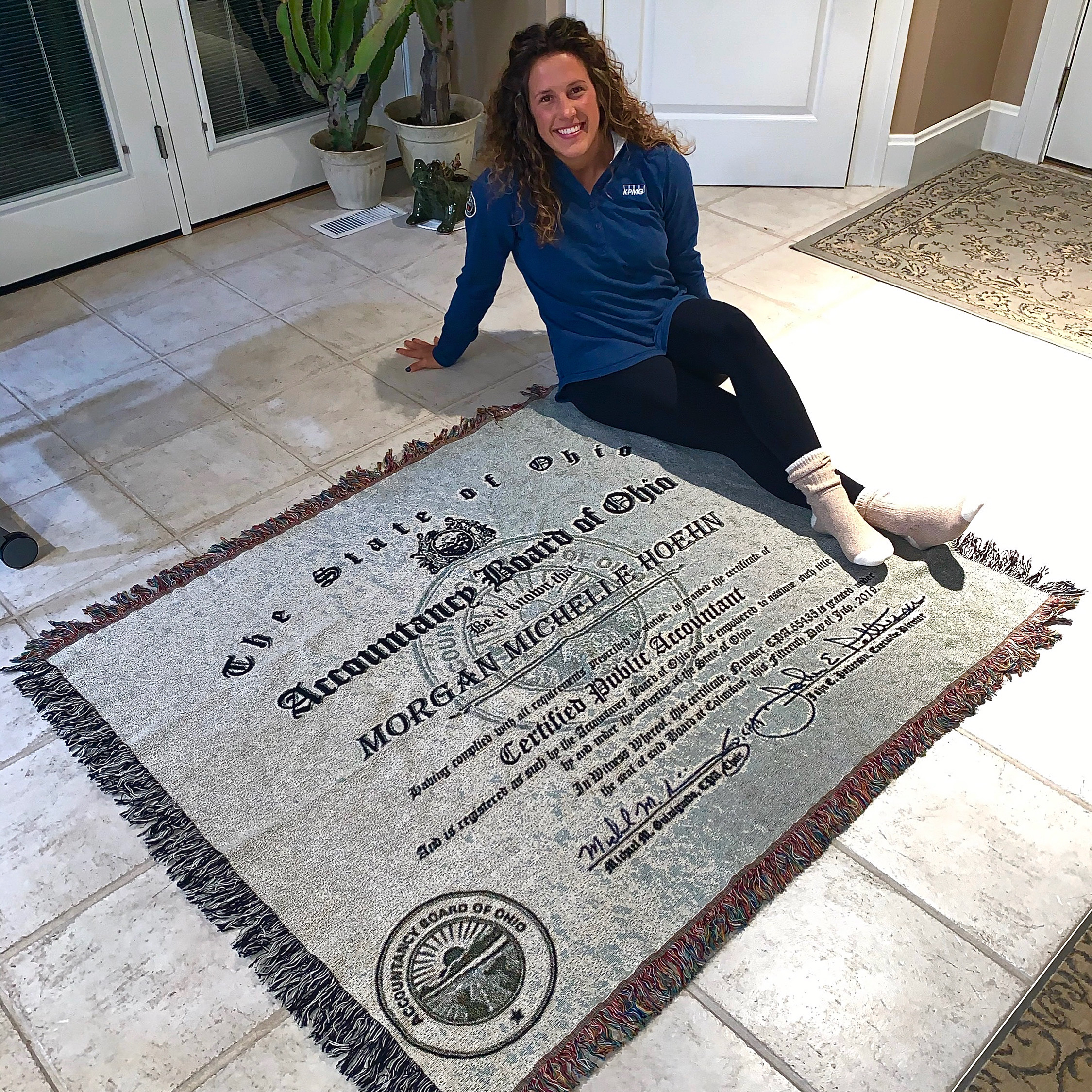 Woman sits on floor with a blanket that has her CPA certificate printed on it.